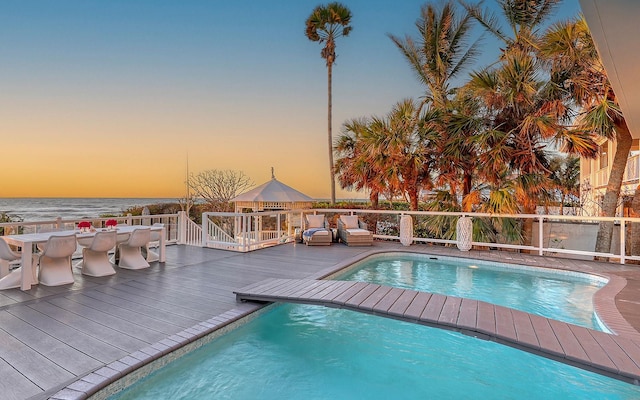 pool at dusk featuring a deck with water view