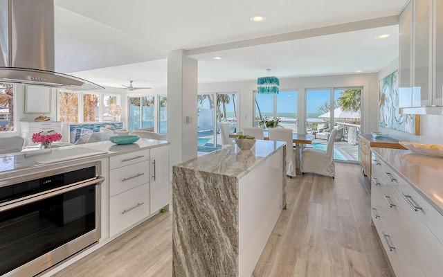 kitchen with light stone counters, island range hood, white cabinetry, and stainless steel oven