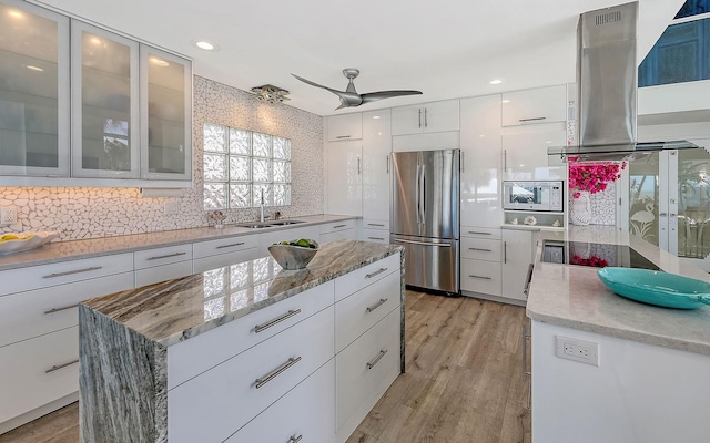 kitchen with extractor fan, sink, a center island, white cabinetry, and stainless steel refrigerator