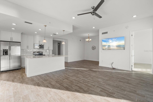 kitchen with pendant lighting, hardwood / wood-style floors, a kitchen island with sink, white cabinets, and appliances with stainless steel finishes