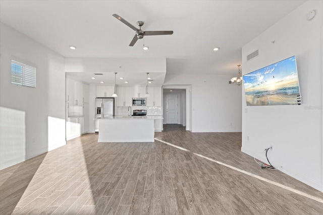 unfurnished living room with sink, light hardwood / wood-style floors, and ceiling fan with notable chandelier