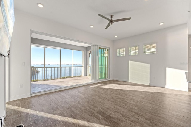 unfurnished room with ceiling fan, a water view, and light wood-type flooring