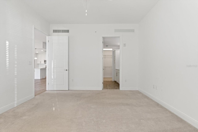 unfurnished bedroom featuring light colored carpet and a walk in closet