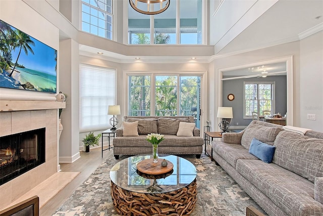 living room with a chandelier, a towering ceiling, light wood-type flooring, and a tiled fireplace