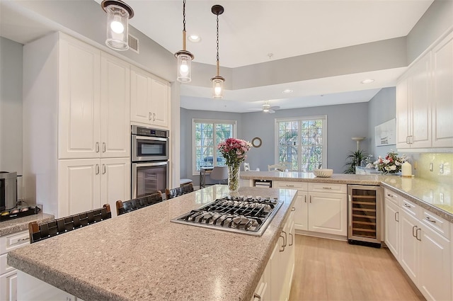 kitchen with kitchen peninsula, hanging light fixtures, appliances with stainless steel finishes, white cabinetry, and beverage cooler