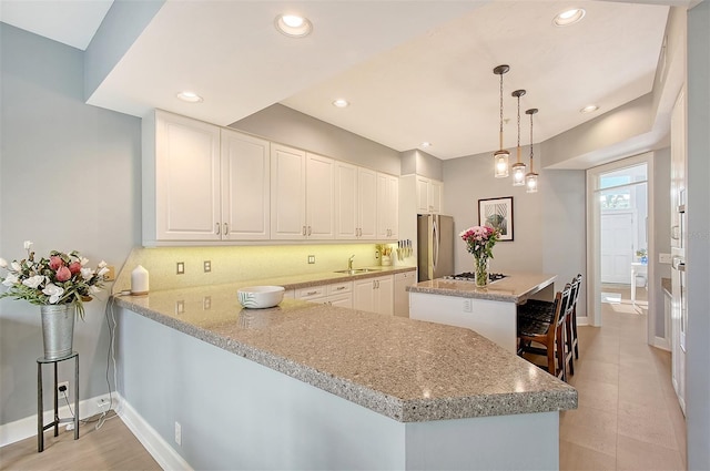 kitchen featuring kitchen peninsula, stainless steel fridge, light stone countertops, white cabinetry, and hanging light fixtures