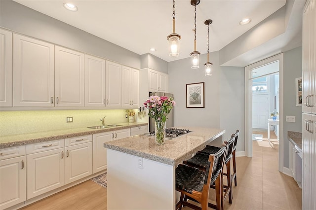 kitchen featuring a center island, light stone counters, white cabinetry, and sink