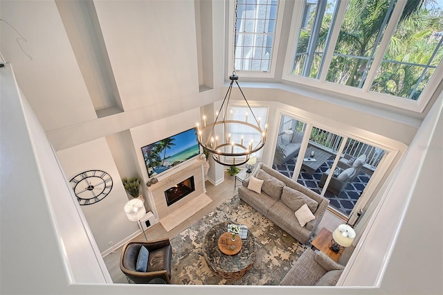 living room with wood-type flooring, a towering ceiling, a high end fireplace, and an inviting chandelier