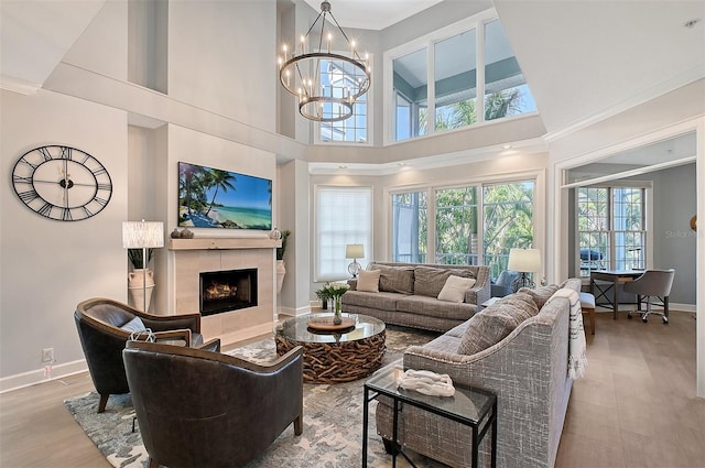 living area with a notable chandelier, a fireplace, wood finished floors, baseboards, and ornamental molding