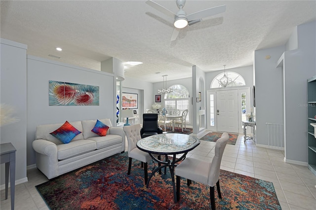 living room featuring light tile patterned flooring, ceiling fan with notable chandelier, and a textured ceiling