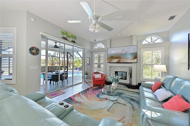 tiled living room with ceiling fan, a fireplace, and a healthy amount of sunlight