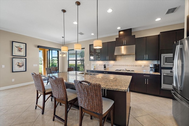 kitchen featuring pendant lighting, sink, light tile patterned floors, an island with sink, and appliances with stainless steel finishes