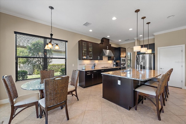 kitchen with appliances with stainless steel finishes, light stone counters, sink, a center island with sink, and hanging light fixtures