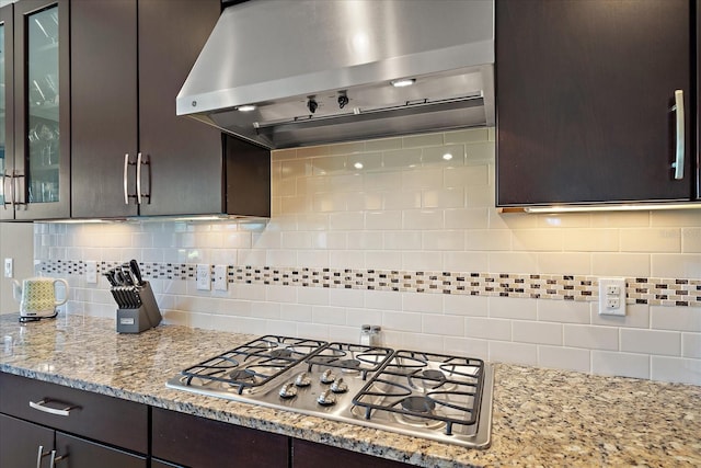 kitchen featuring decorative backsplash, dark brown cabinets, wall chimney range hood, and stainless steel gas cooktop