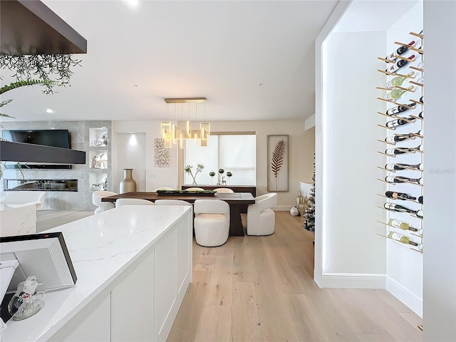 kitchen featuring pendant lighting, white cabinets, light stone countertops, light wood-type flooring, and a notable chandelier