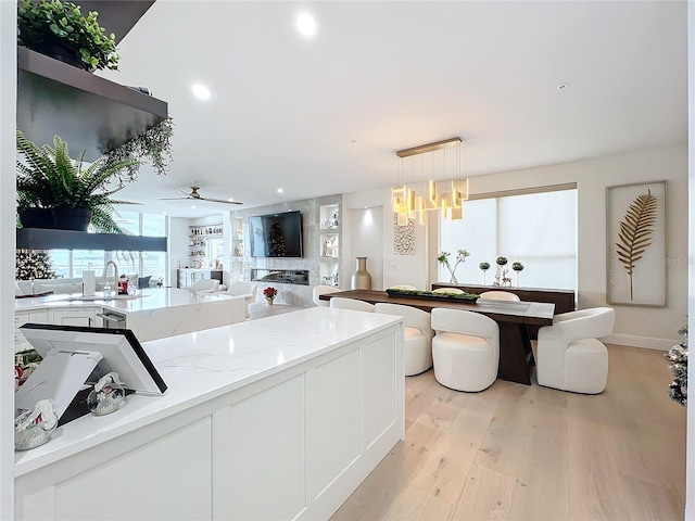 kitchen featuring light stone counters, ceiling fan with notable chandelier, white cabinets, light hardwood / wood-style floors, and hanging light fixtures