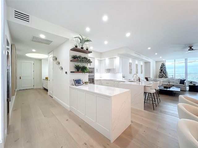 kitchen with white cabinetry, ceiling fan, sink, light hardwood / wood-style flooring, and kitchen peninsula