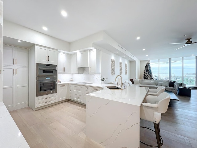 kitchen with light stone countertops, sink, backsplash, kitchen peninsula, and white cabinets