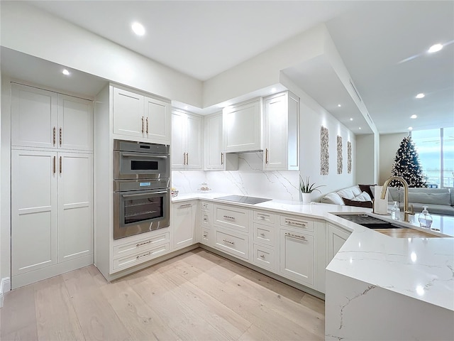 kitchen featuring white cabinets, sink, light stone countertops, double oven, and light hardwood / wood-style floors