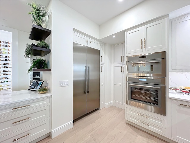 kitchen featuring light stone countertops, tasteful backsplash, light hardwood / wood-style floors, white cabinets, and appliances with stainless steel finishes