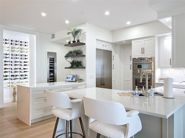 kitchen with a large island with sink, tasteful backsplash, white cabinetry, and appliances with stainless steel finishes