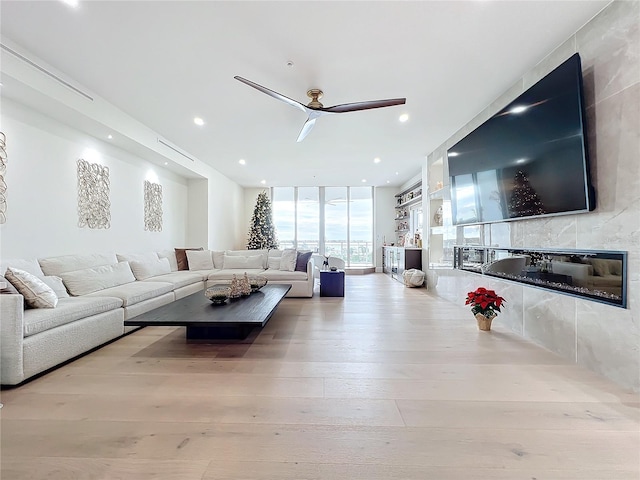 living room featuring a tile fireplace, expansive windows, light hardwood / wood-style floors, and ceiling fan