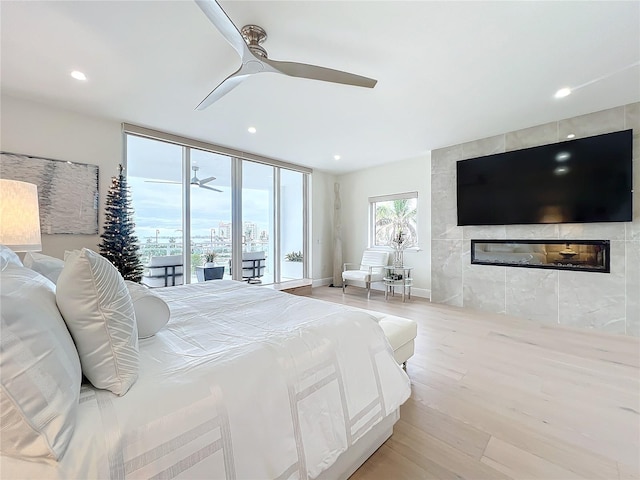 bedroom featuring ceiling fan, access to exterior, a tile fireplace, and light hardwood / wood-style flooring