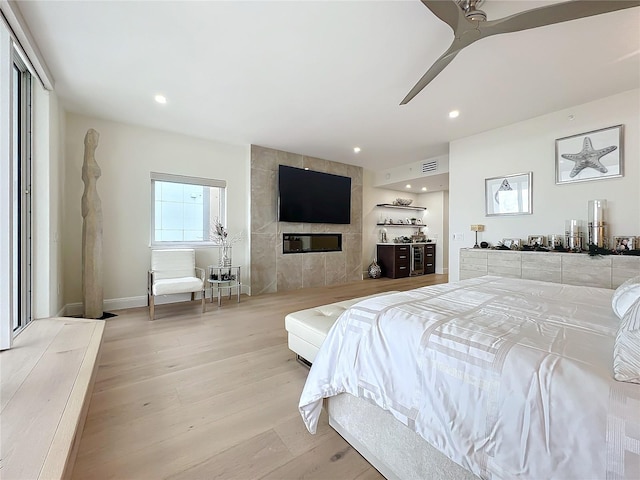 bedroom with a tile fireplace, light wood-type flooring, and ceiling fan