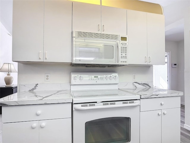 kitchen with hardwood / wood-style floors, light stone counters, and white appliances