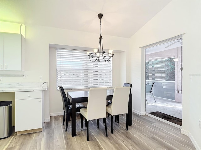 dining area with a notable chandelier, light hardwood / wood-style floors, a wealth of natural light, and vaulted ceiling