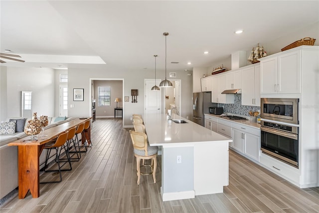 kitchen with a breakfast bar area, a sink, light countertops, appliances with stainless steel finishes, and a center island with sink