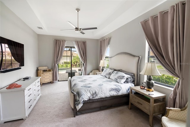 bedroom featuring ceiling fan, light colored carpet, visible vents, access to exterior, and a tray ceiling