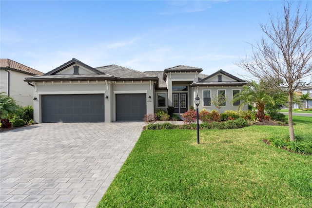 prairie-style house featuring a garage, decorative driveway, a front lawn, and stucco siding