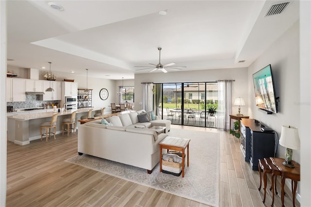 living room featuring light wood finished floors, ceiling fan, visible vents, and a tray ceiling