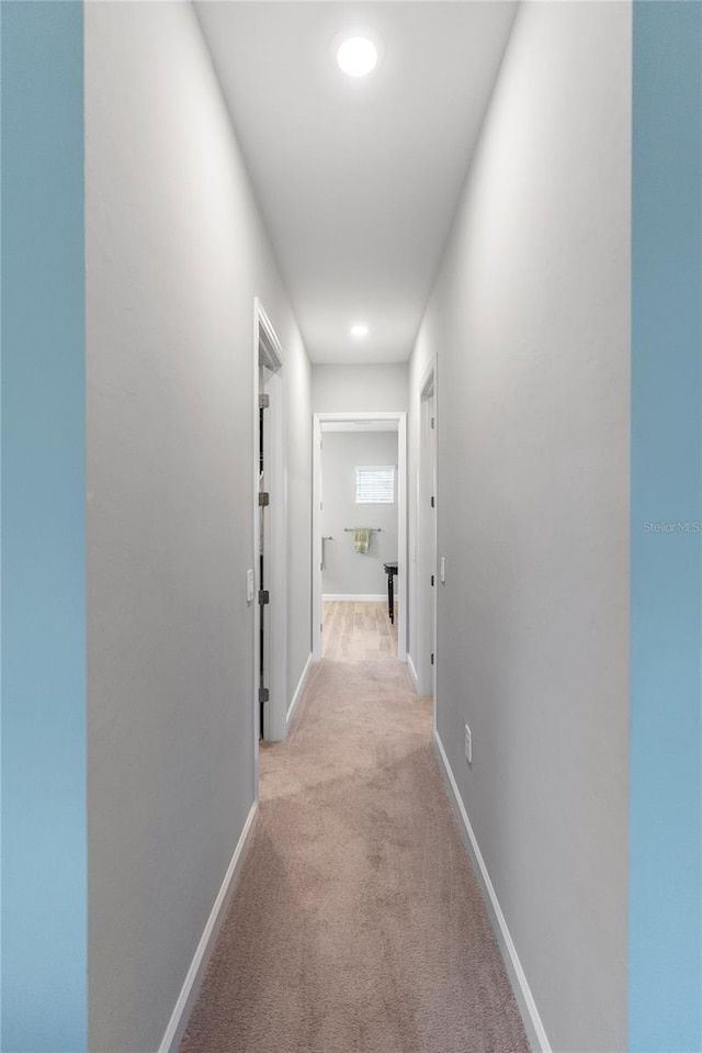 corridor featuring baseboards and light colored carpet