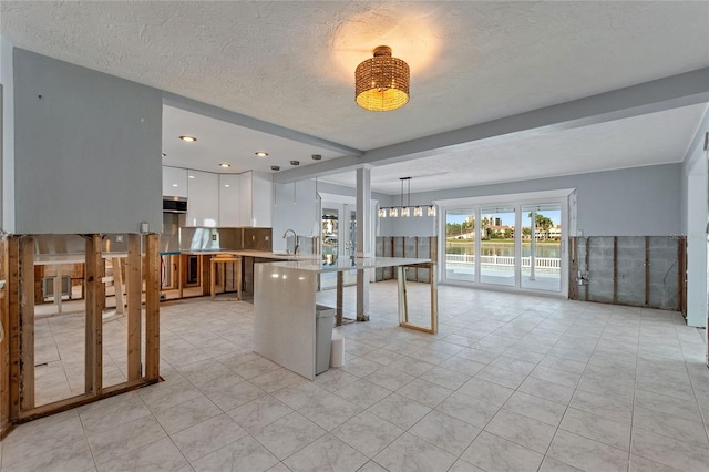 kitchen with a breakfast bar, a textured ceiling, sink, pendant lighting, and white cabinets