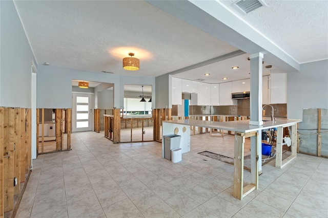 kitchen featuring kitchen peninsula, a textured ceiling, sink, light tile patterned floors, and white cabinets