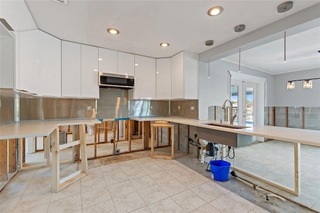 kitchen with tasteful backsplash, sink, decorative light fixtures, white cabinetry, and light tile patterned flooring