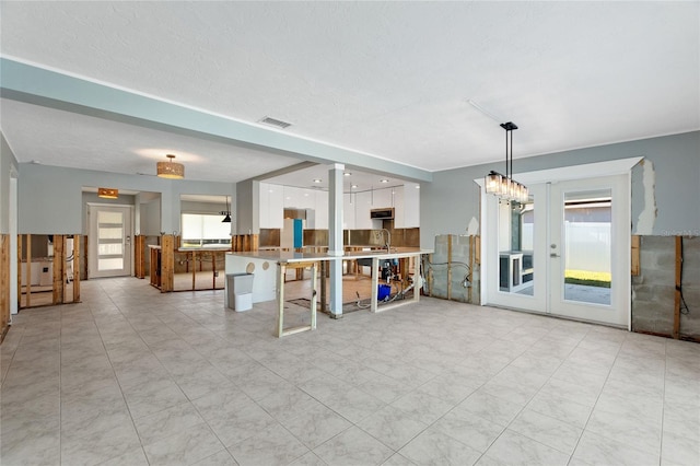 kitchen with french doors, kitchen peninsula, a textured ceiling, decorative light fixtures, and white cabinetry