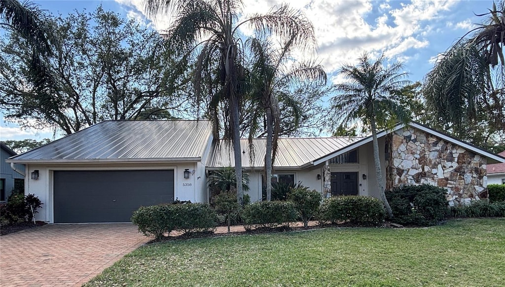 view of front facade featuring metal roof, an attached garage, decorative driveway, a front lawn, and stucco siding