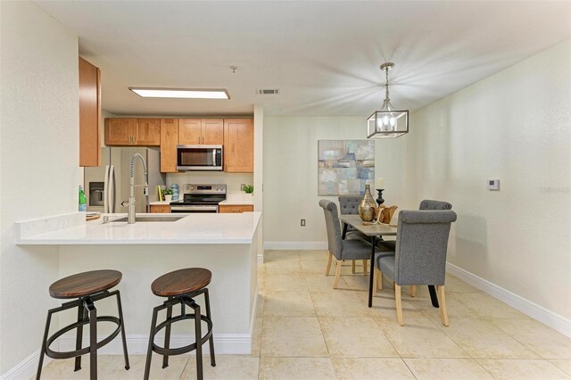 kitchen with hanging light fixtures, kitchen peninsula, a breakfast bar area, light tile patterned flooring, and appliances with stainless steel finishes