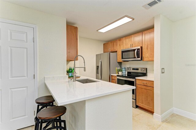 kitchen with light stone countertops, sink, stainless steel appliances, kitchen peninsula, and a breakfast bar