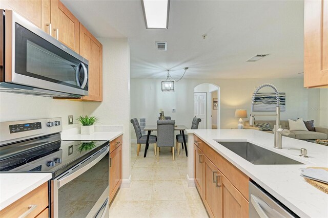 kitchen with appliances with stainless steel finishes, light tile patterned floors, an inviting chandelier, and sink