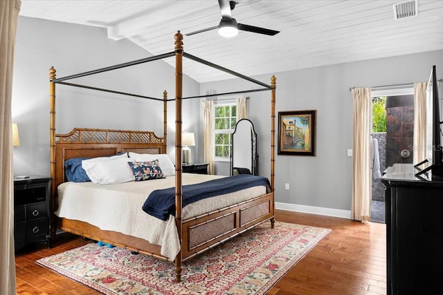 bedroom featuring ceiling fan, multiple windows, hardwood / wood-style flooring, and vaulted ceiling with beams