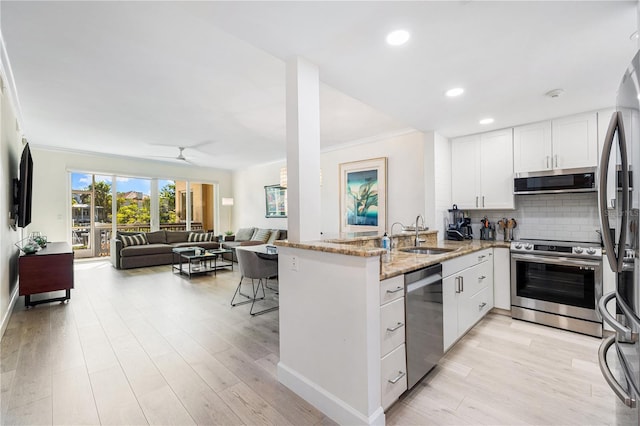 kitchen with kitchen peninsula, sink, white cabinetry, light stone countertops, and appliances with stainless steel finishes