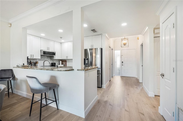 kitchen featuring white cabinets, stainless steel appliances, dark stone counters, decorative backsplash, and kitchen peninsula