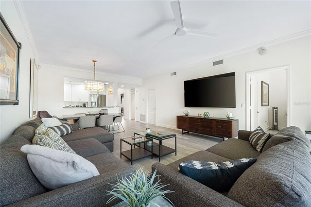 living room featuring light wood-type flooring, ornamental molding, and ceiling fan with notable chandelier