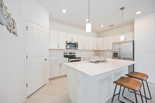 kitchen with appliances with stainless steel finishes, sink, decorative light fixtures, white cabinets, and an island with sink