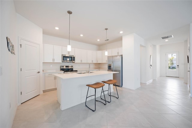 kitchen with white cabinetry, sink, hanging light fixtures, stainless steel appliances, and a kitchen island with sink