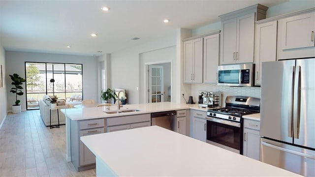 kitchen featuring sink, light wood-type flooring, tasteful backsplash, kitchen peninsula, and stainless steel appliances